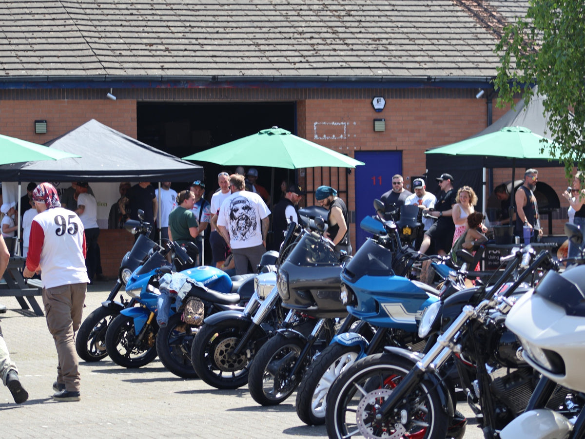 Motorcycle line-up with event guests gathered outside the workshop.