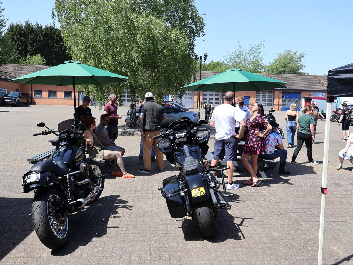 Motorcycles and guests around picnic tables at the shop opening party.