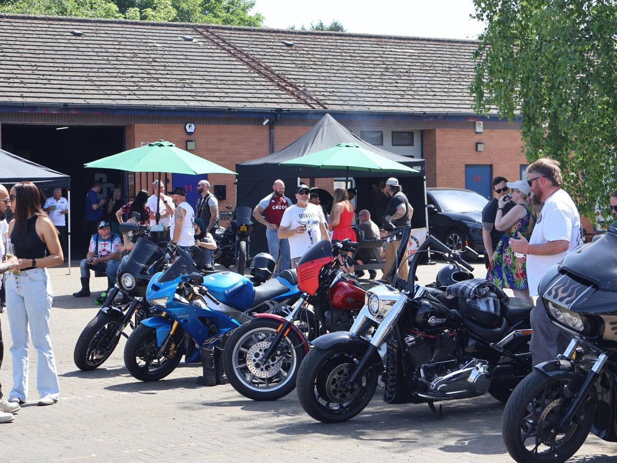 Motorcycles lined up outside the workshop with riders socialising at a Deathproof event.