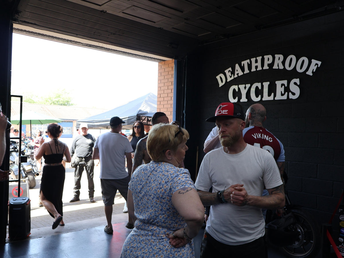 Guests chatting inside the workshop beneath the Deathproof Cycles sign.