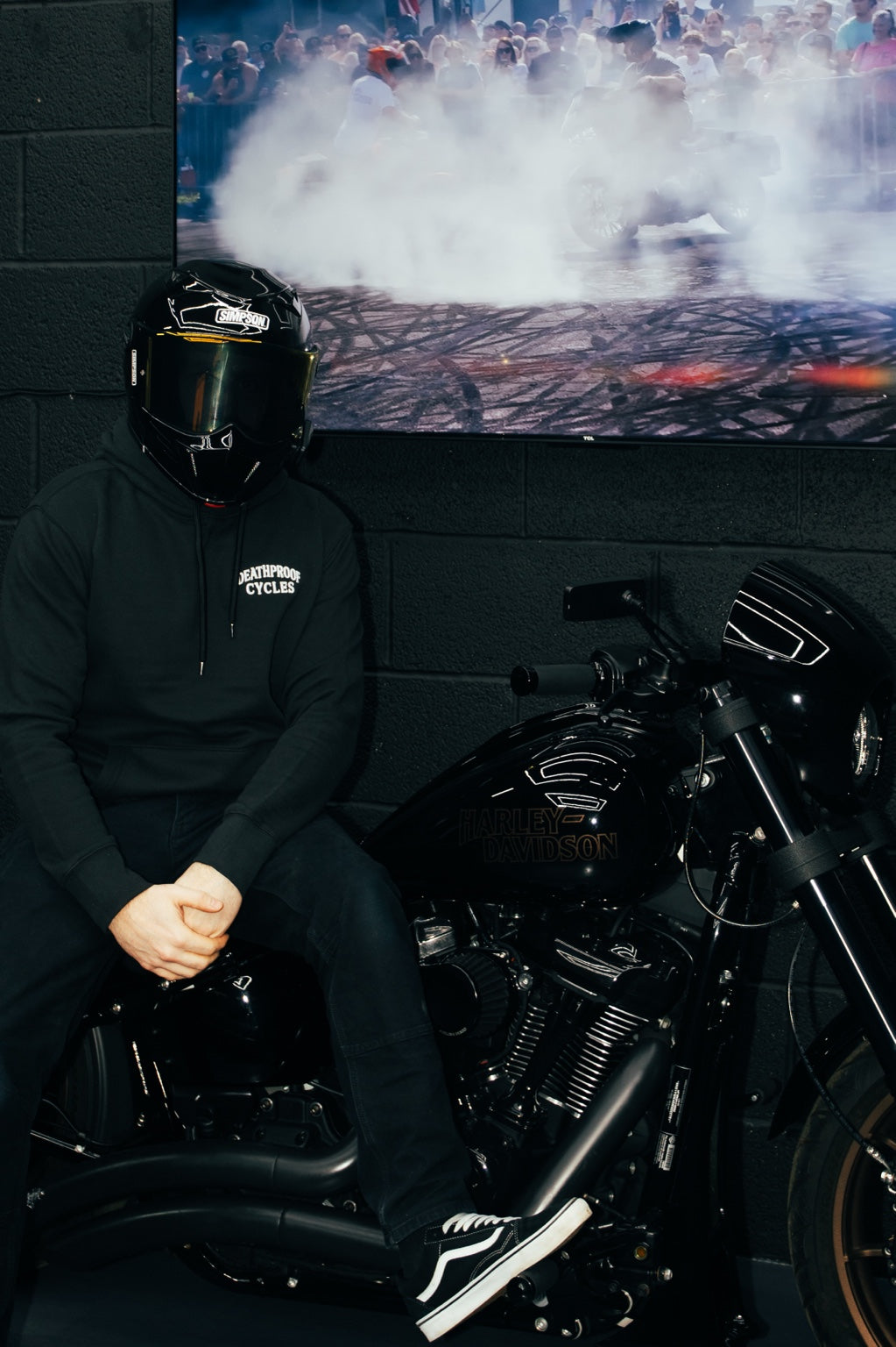 Rider in a Deathproof hoodie beside a Harley